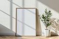 Frame mockup picture on wood floor against white wall, detail of modern minimalist room interior with blank poster and plant. Royalty Free Stock Photo