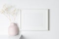 Frame mockup on white wall with dry flowers in vase, blank mockup for print presentation