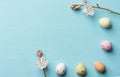 Frame from multicolored speckled chocolate eggs spring field flowers on light blue background with linen paper texture. Easter