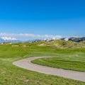 Frame Square Vast grassy field with a curving paved road and houses beyond the slopes Royalty Free Stock Photo