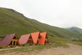 a-frame triangular houses in mountains, around rocks and green grass