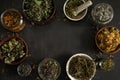 Frame of various dried herbs in cups on a dark concrete background.