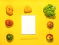 Frame of vegetables and fruits around empty clean white notepad on bright yellow background with copy space for text