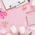 Frame with white flowers, mug of coffee, clipboard, clips and glasses on pink background. Flat lay, top view