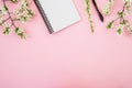 Frame of white flowers, notebook and pen on pink background. Flat lay, top view. Blogger or freelancer desk workspace.