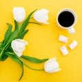 Frame of white tulips flowers with mug of coffee and marshmallows on yellow background. Floral concept. Flat lay, top view. Royalty Free Stock Photo