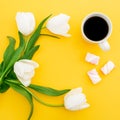 Frame of white tulips flowers with mug of coffee and marshmallows on yellow background. Floral concept. Flat lay, top view. Royalty Free Stock Photo