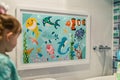 framed artwork of cartoon sea creatures on a bathroom wall near a child Royalty Free Stock Photo