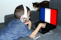 France flag on laptop display, little schoolboy in jeans lies on a sofa and scrolls, a cat sits nearby, a concept of studying