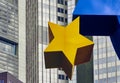 Detail of a yellow star of the Euro sculpture with the old former building of the European Central Bank ECB in the background
