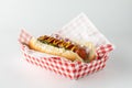 A frankfurter in a disposable checkered tray isolated against a white background.