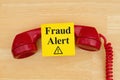 Fraud alert on sticky note with a retro red phone on textured wood desk