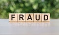 FRAUD word written on wooden blocks. The text is written in black letters and is reflected in the mirror surface of the table Royalty Free Stock Photo