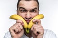 A freak man in white shirt is holding two bananas close to his face and making funny faces. This vegan likes to eat