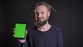 Freaky caucasian man with dreadlocks working with tablet and smilingly showing its display to camera on black background