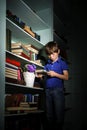 Freckled red-haired little boy searching book on bookcase