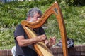 Closeup image of a street musician performing on the sidewalk by playing his harp.