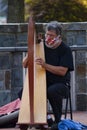 An elderly street performer wearing face mask is playing harp