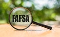 Free Application for Federal Student Aid - FAFSA written on magnifying glass on wooden table and green background. Concept image