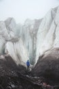 A free climber with an ice ax stands at the foot of the Great Glacier next to an epic crack in the fog in the mountains