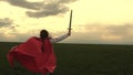 Free girl in a red cloak runs with swords in his hand across field playing medieval knight. young girl playing super Royalty Free Stock Photo