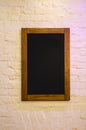 Empty black billboard in a wooden frame on a white brick wall