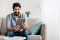 Free time concept. Portrait of happy guy using digital tablet sitting on the sofa at home, free space Royalty Free Stock Photo