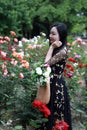 Beautiful young woman with book and bag visiting a rose garden . Royalty Free Stock Photo