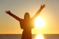 Free woman raising arms watching sun at sunrise