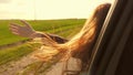 Free woman travels by car catches the wind with her hand from the car window. Girl with long hair is sitting in front