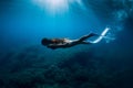 Freediver girl with white fins glides underwater with amazing sun rays and seaweed. Free diving underwater in blue sea Royalty Free Stock Photo