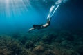 Freediver girl with white fins glides underwater with amazing sun rays and seaweed. Free diving underwater in blue sea Royalty Free Stock Photo