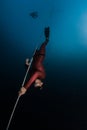 Freediver in red wetsuit descends along the rope