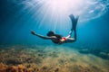 Freediver woman in bikini glides in blue sea and sun rays. Freediving with fins underwater in ocean