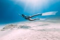 Freediver underwater glides with white fins. Attractive woman freediver in blue ocean with sun rays