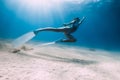 Freediver underwater glides with white fins over sandy bottom. Attractive woman freediver in blue ocean with sun rays Royalty Free Stock Photo