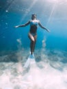 Freediver woman glides and posing over sandy sea with white freediving fins