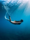 Freediver young woman with white fins glides undersea with sun rays. Freediving in transparent sea