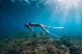 Freediver young woman with white fins glides undersea with sun rays. Freediving in transparent sea