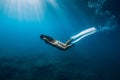 Freediver young woman with white fins glides undersea with sun rays. Freediving in transparent sea