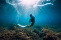 Freediver young woman with white fins glides undersea with sun rays. Freediving in transparent sea