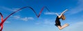 Jymnast with red ribbon jumping against blue sky Royalty Free Stock Photo