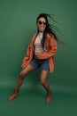 Emotional african girl in shorts and shirt dancing, having fun isolated on dark green background. Concept of beauty, art Royalty Free Stock Photo