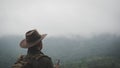 Freedom traveler man in hat carrying a backpack stands at the top of a mountain and using a smartphone on a foggy day.Adventure