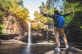 Freedom traveler woman standing waterfall front on stone with bag and raised arms enjoying a beautiful nature. Royalty Free Stock Photo