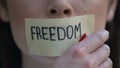 Freedom written on tape, woman removing mouth sticker, rights oppression, block