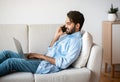 Freelance. Handsome Arab Man Using Laptop And Talking On Cellphone At Home Royalty Free Stock Photo