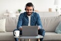Freelance job. Young smiling Arab man working on laptop from home, wearing headphones, using pc computer Royalty Free Stock Photo