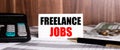 FREELANCE JOBS written on a white card near a calculator and coins on a wooden background. Business concept