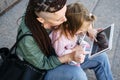 Freelance Parents. Busy working mom with baby toddler daughter on hands walk and looking on tablet in street Royalty Free Stock Photo